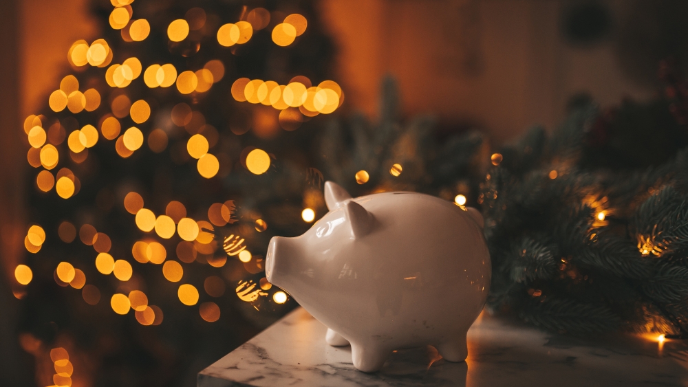 ceramic piggy bank in front of christmas tree with fairy lights twinkling.