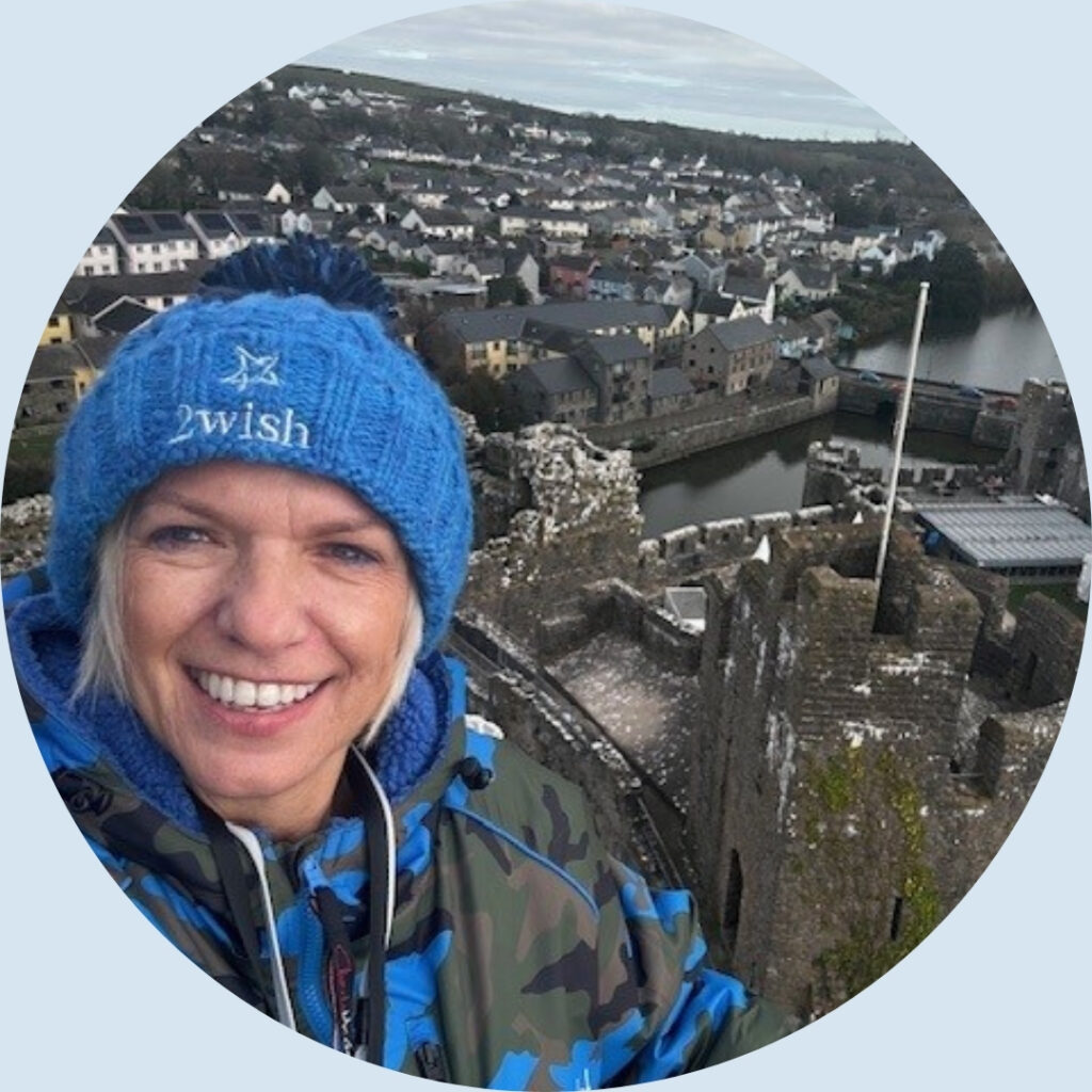 woman wearing 2wish branded bobble hat smiling at camera with pembroke castle behind her