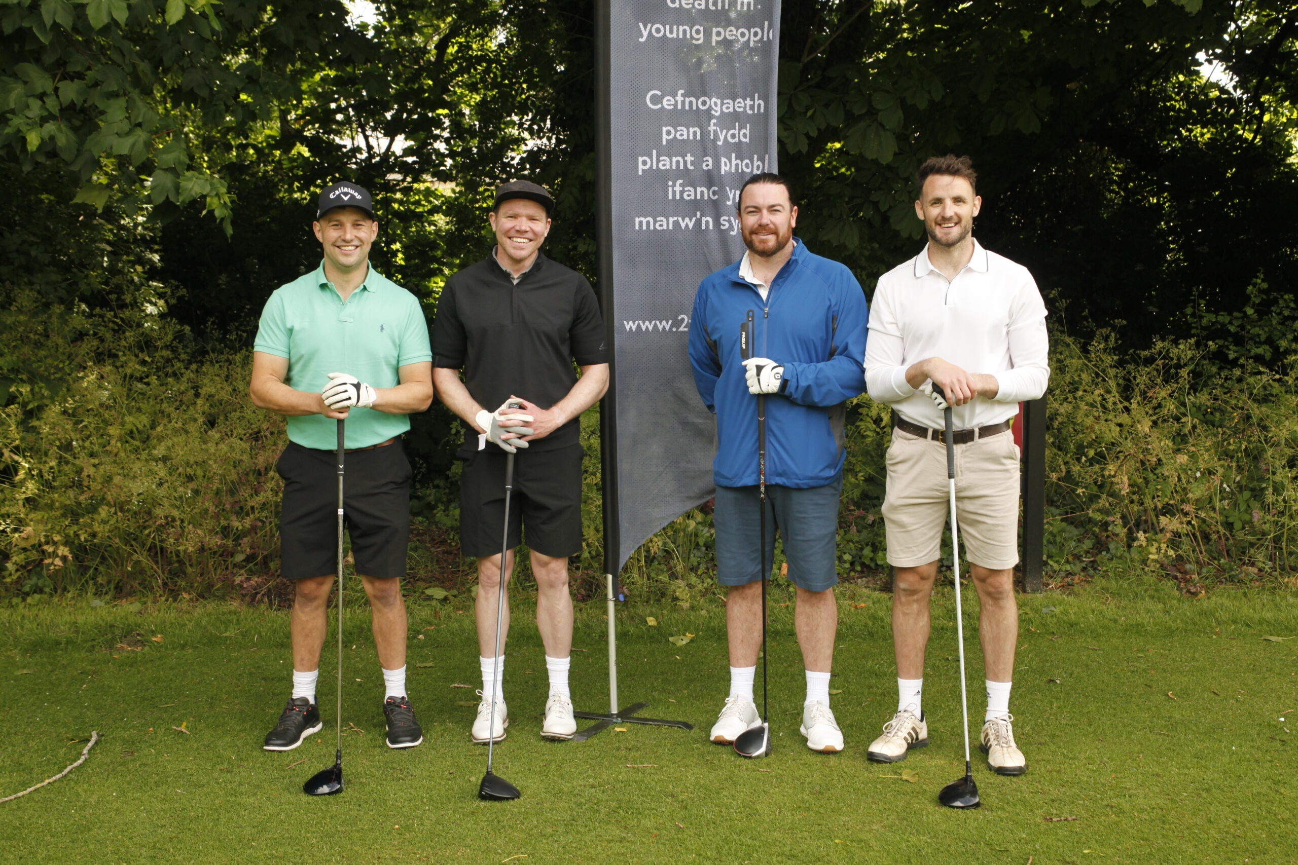 4 men standing by a 2wish flag with golf clubs